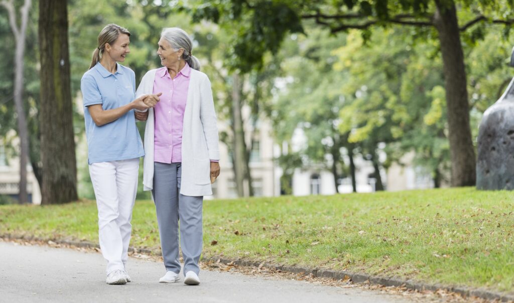 Betreuungskraft geht mit älterer Dame die Straße entlang